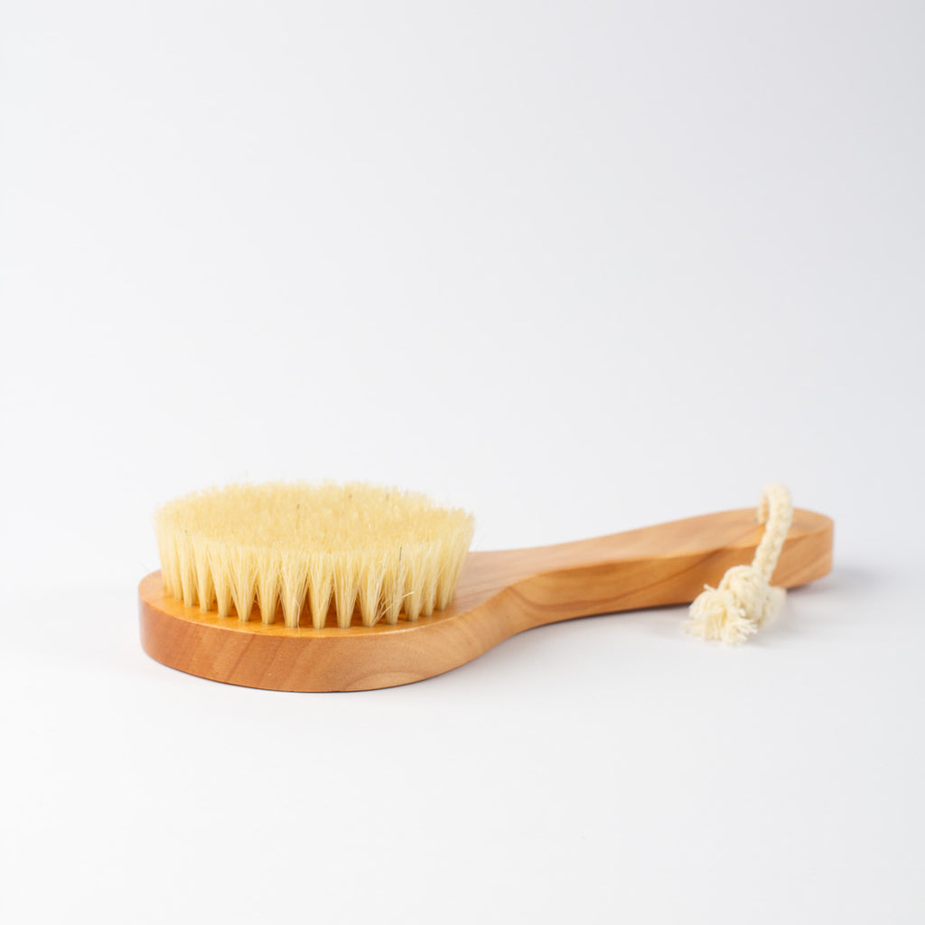 A wooden body brush with natural beige bristles and a knotted rope handle, photographed on a clean white background.