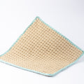 A square crocheted washcloth in a natural beige yarn, finished with a sage green crochet border, shown on a clean white background.