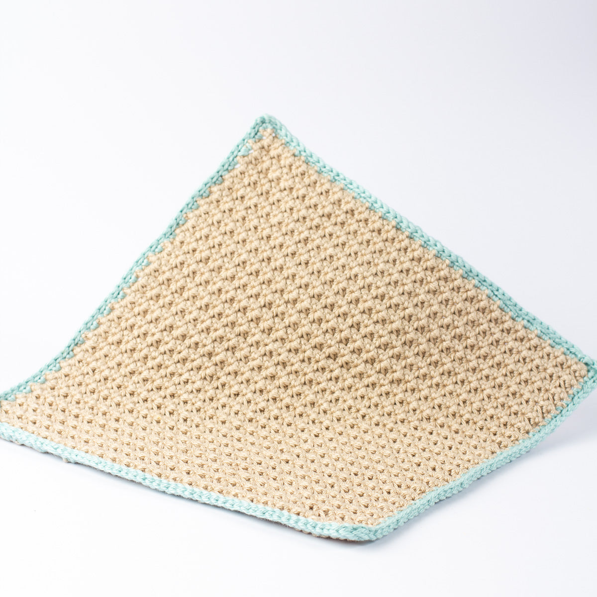 A square crocheted washcloth in a natural beige yarn, finished with a sage green crochet border, shown on a clean white background.