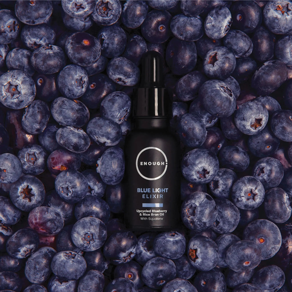 Black bottle of 'Enough' Blue Light Elixir surrounded by blueberries