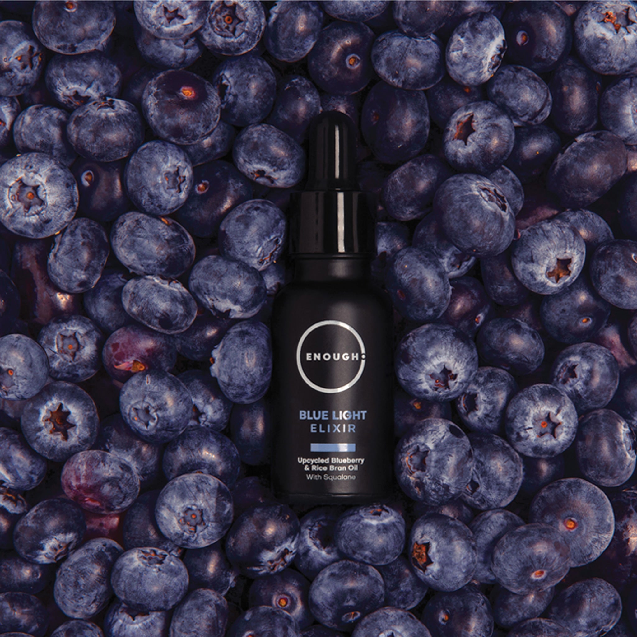 Black bottle of 'Enough' Blue Light Elixir surrounded by blueberries
