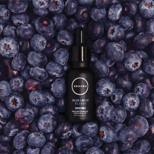 Black bottle of 'Enough' Blue Light Elixir surrounded by blueberries
