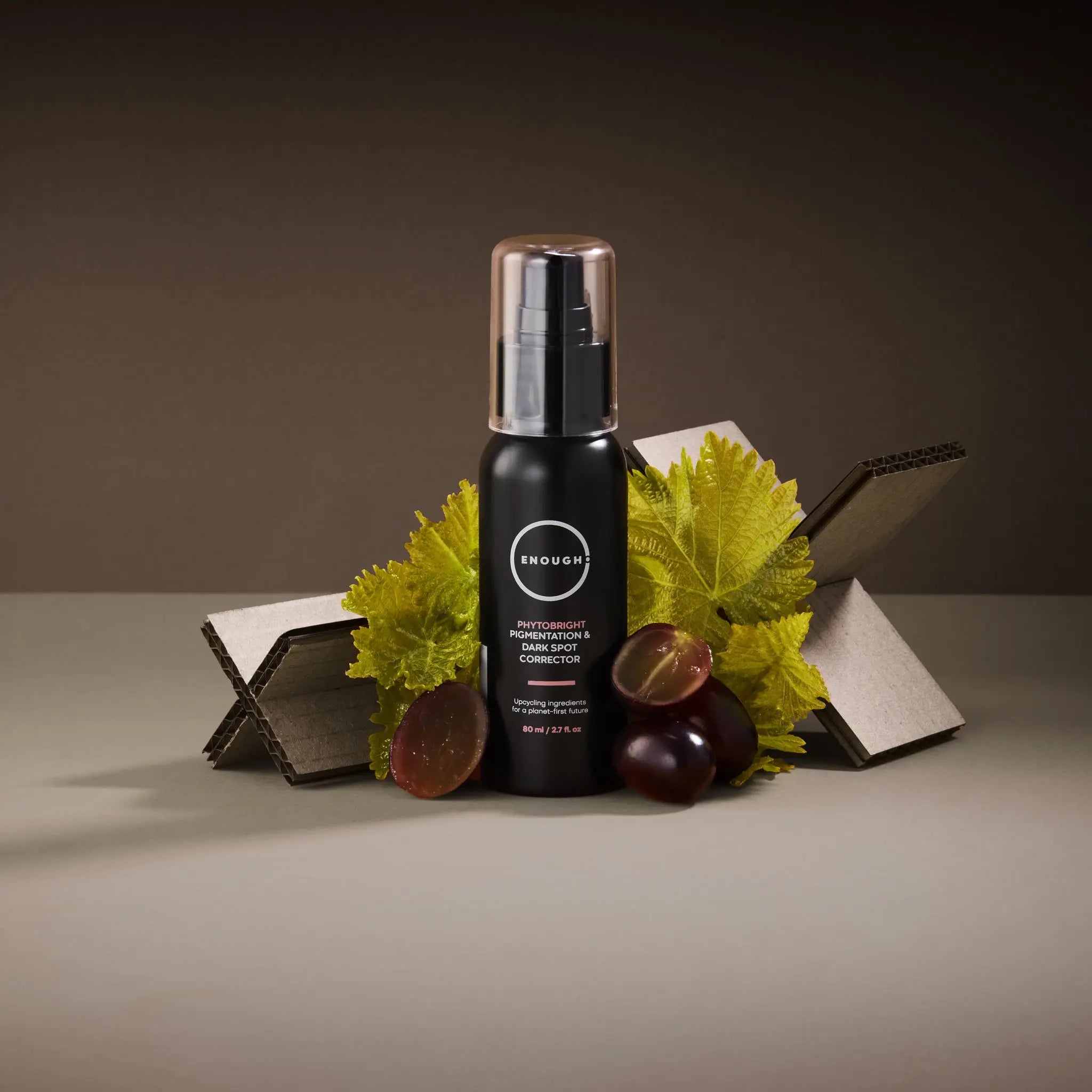 Black bottle containing Phytobright on a gray surface with vine leaves and dark grapes.