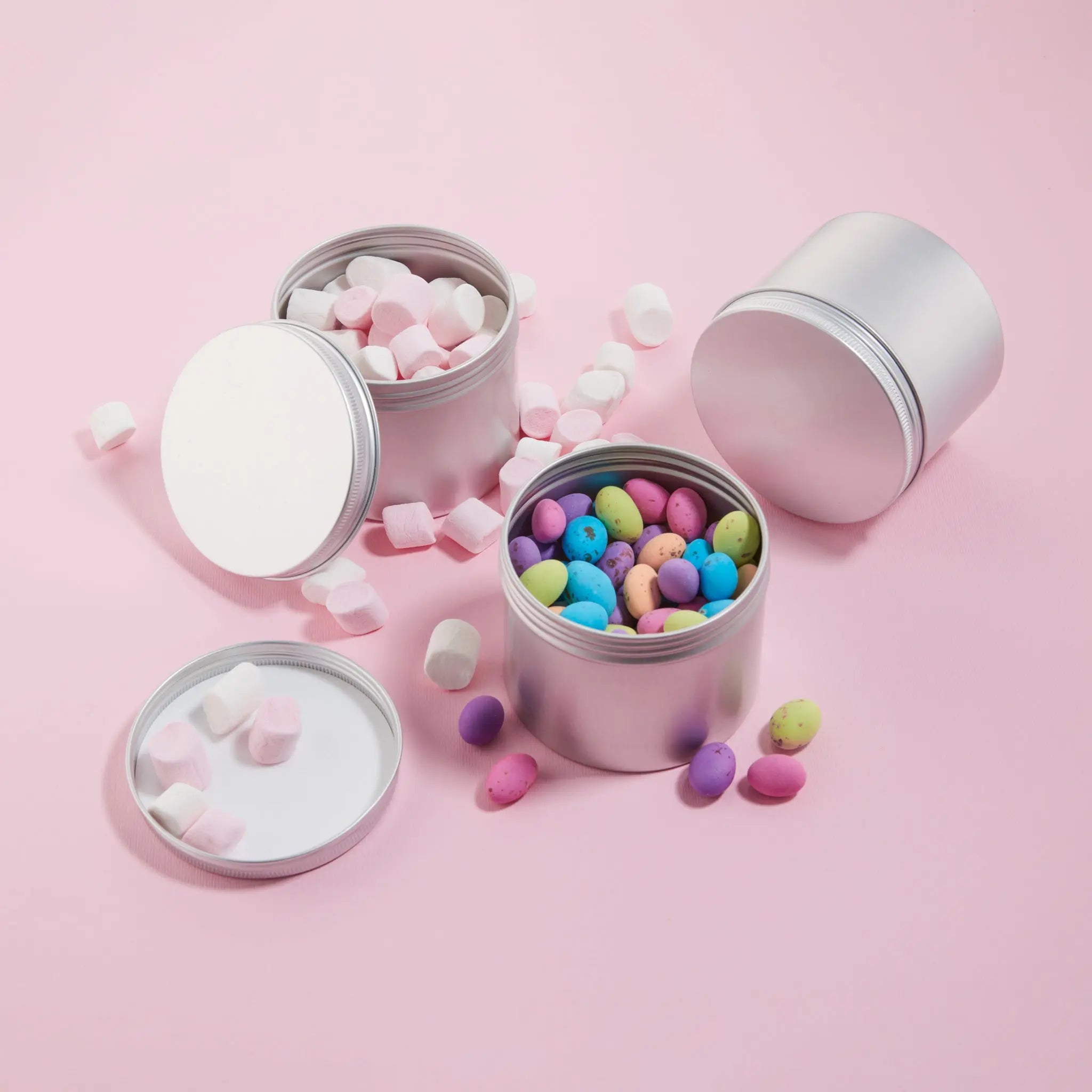 Reusable tins. Silver tins filled with colorful candies on a pink background