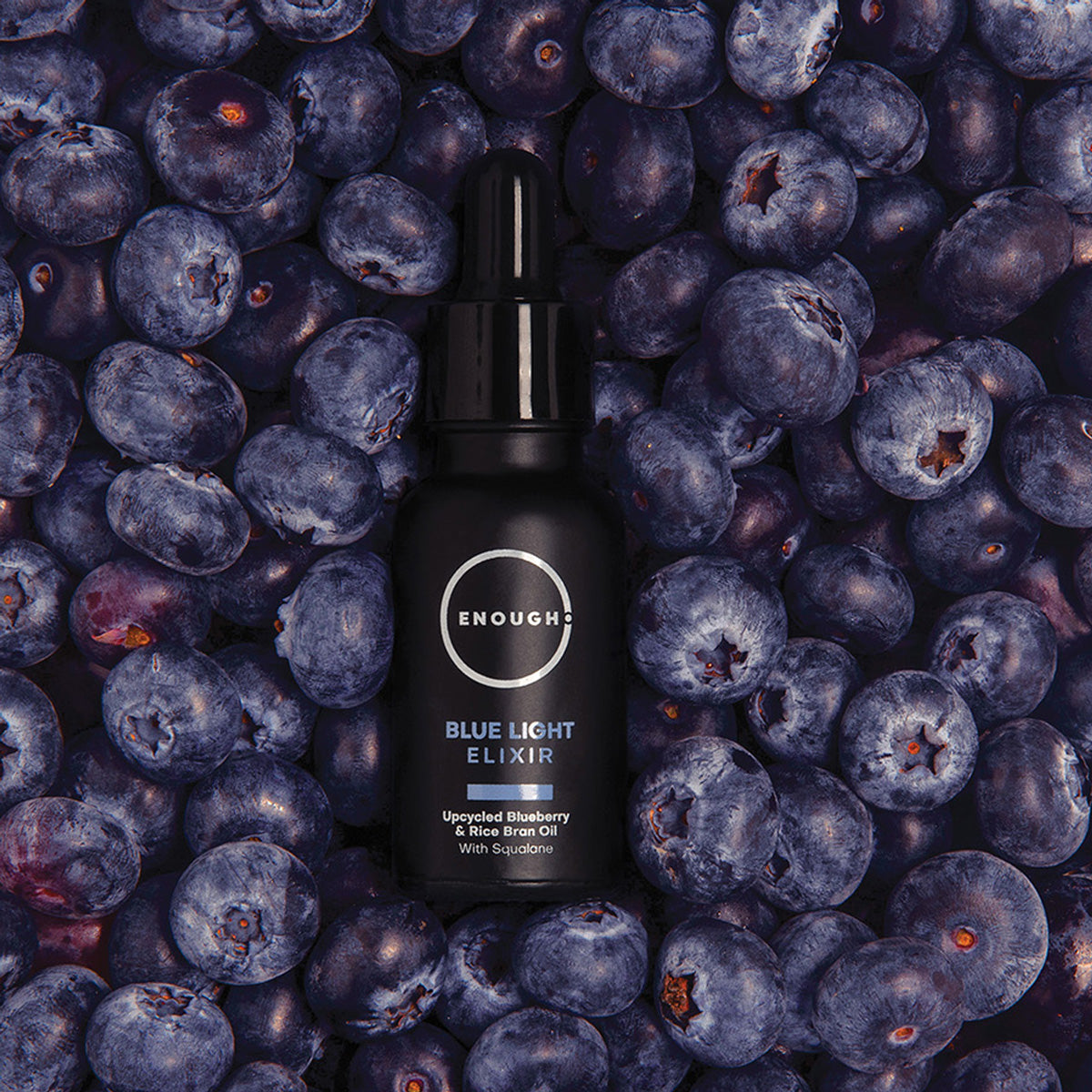 Black bottle of 'Enough' Blue Light Elixir surrounded by blueberries
