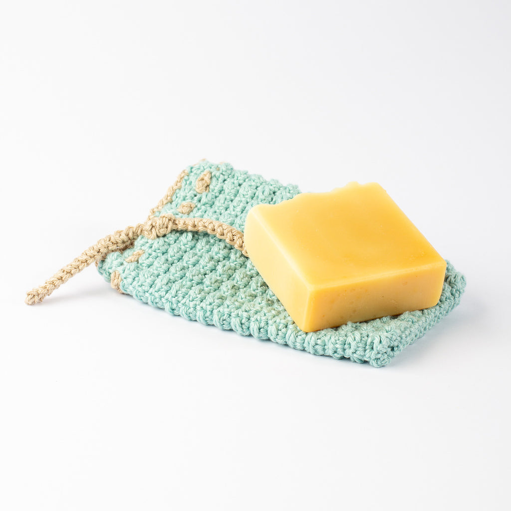 ECONIQUE cotton soap saver bag open flat with golden natural bar soap resting on top, white background