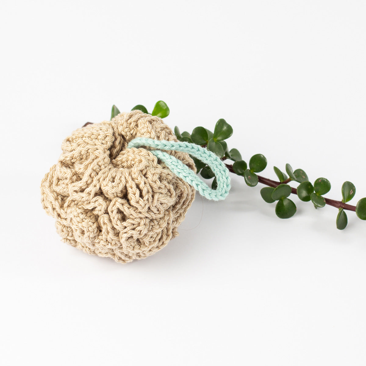 ECONIQUE cotton shower pouffe in natural beige with a small green botanical sprig on a clean white background.