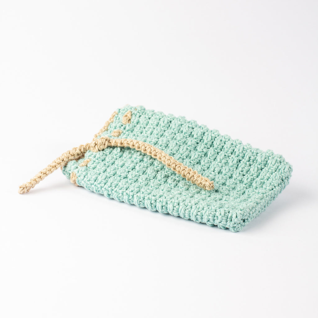 ECONIQUE hand-crocheted natural cotton soap saver bag in sage green with natural beige drawstring, closed, on white surface