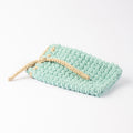 ECONIQUE hand-crocheted natural cotton soap saver bag in sage green with natural beige drawstring, closed, on white surface