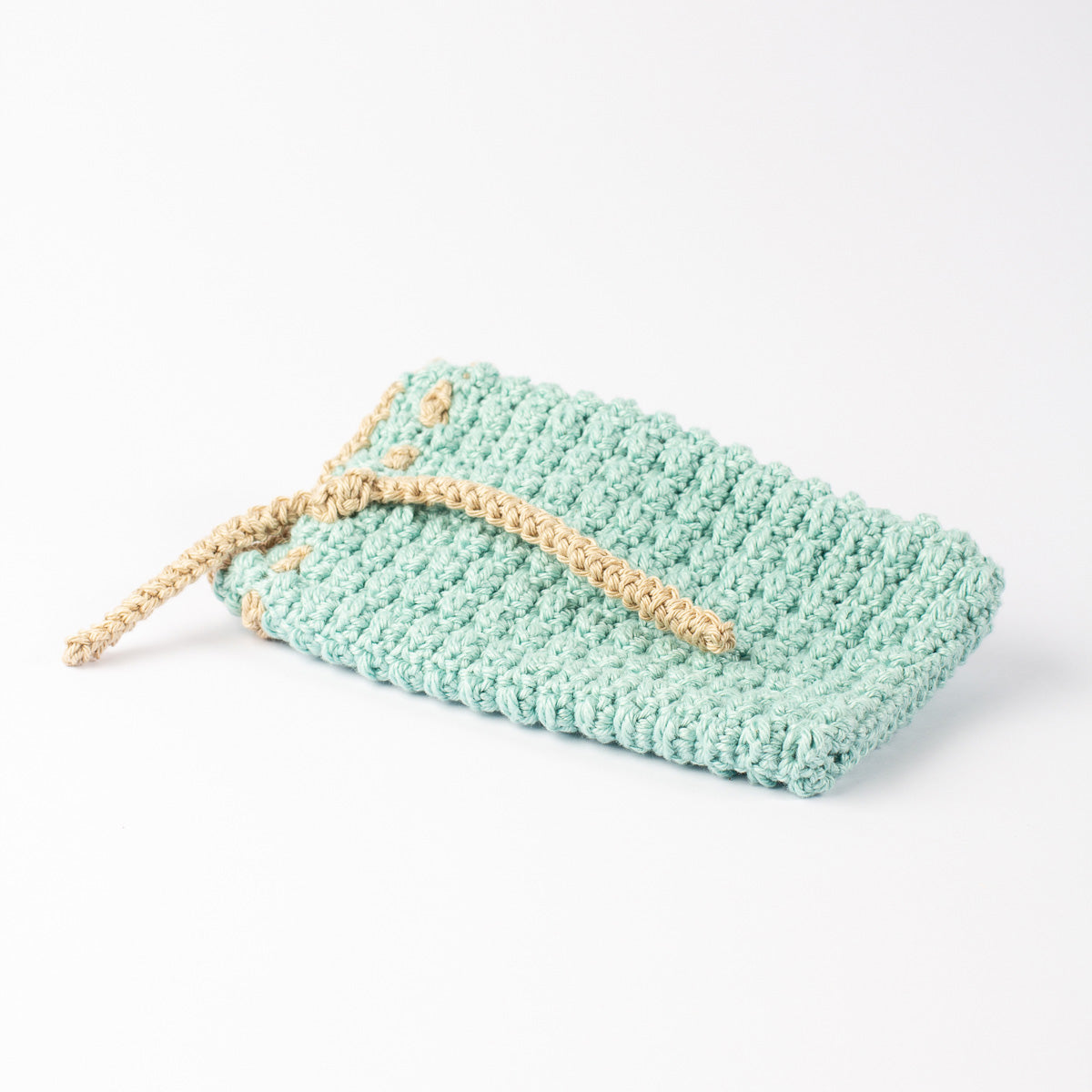 ECONIQUE hand-crocheted natural cotton soap saver bag in sage green with natural beige drawstring, closed, on white surface