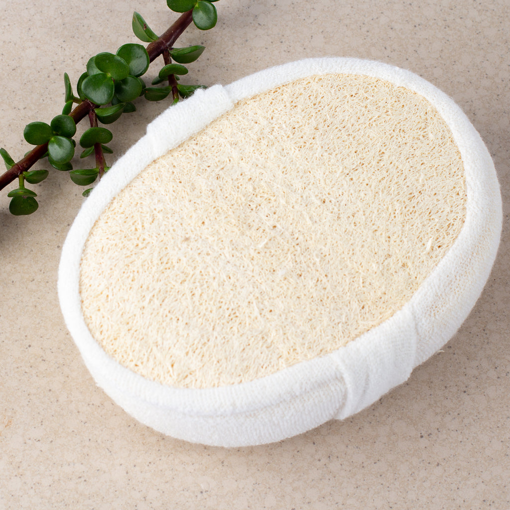 ECONIQUE Natural Exfoliating Loofah Body Sponge showing cream loofah face with open-weave natural fibre texture, photographed from above on a warm stone surface with a succulent sprig