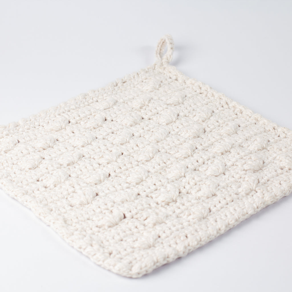 Angled view of ECONIQUE Papyrus white cotton crochet washcloth showing textured body and small hanging loop at top corner