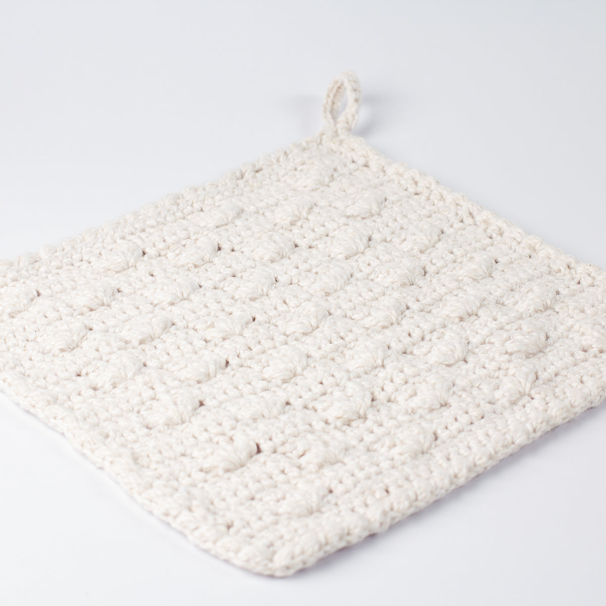 Angled view of ECONIQUE Papyrus white cotton crochet washcloth showing textured body and small hanging loop at top corner