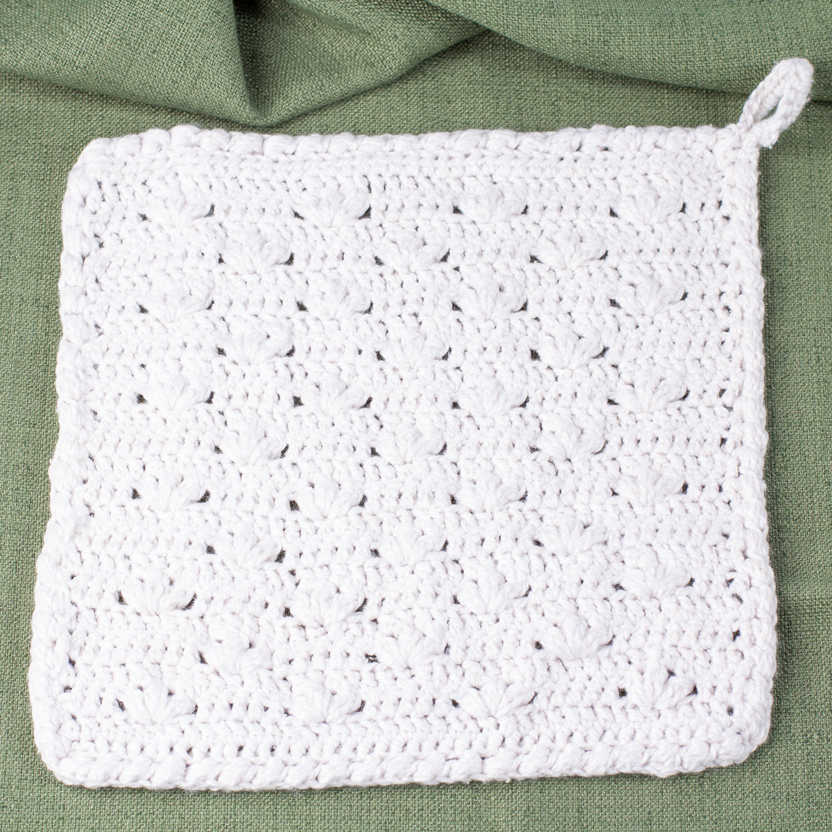 ECONIQUE Papyrus soft cotton washcloth in white styled flat on sage green linen fabric with hanging loop visible